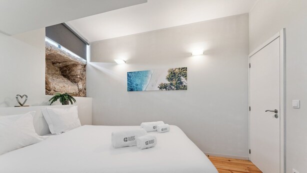 Une chambre moderne avec un grand lit, du linge de lit blanc, un mur en pierre décoratif et deux œuvres d’art accrochées au mur.