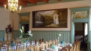 Een elegante eetzaal met decoratieve stoelen, een kroonluchter en een groot schilderij van een stel bij een waterval.