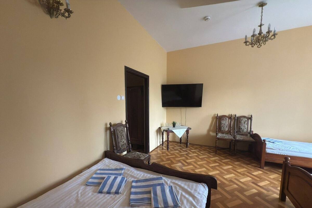 A hotel room with a bed, two chairs, a small table, a TV, and a chandelier.