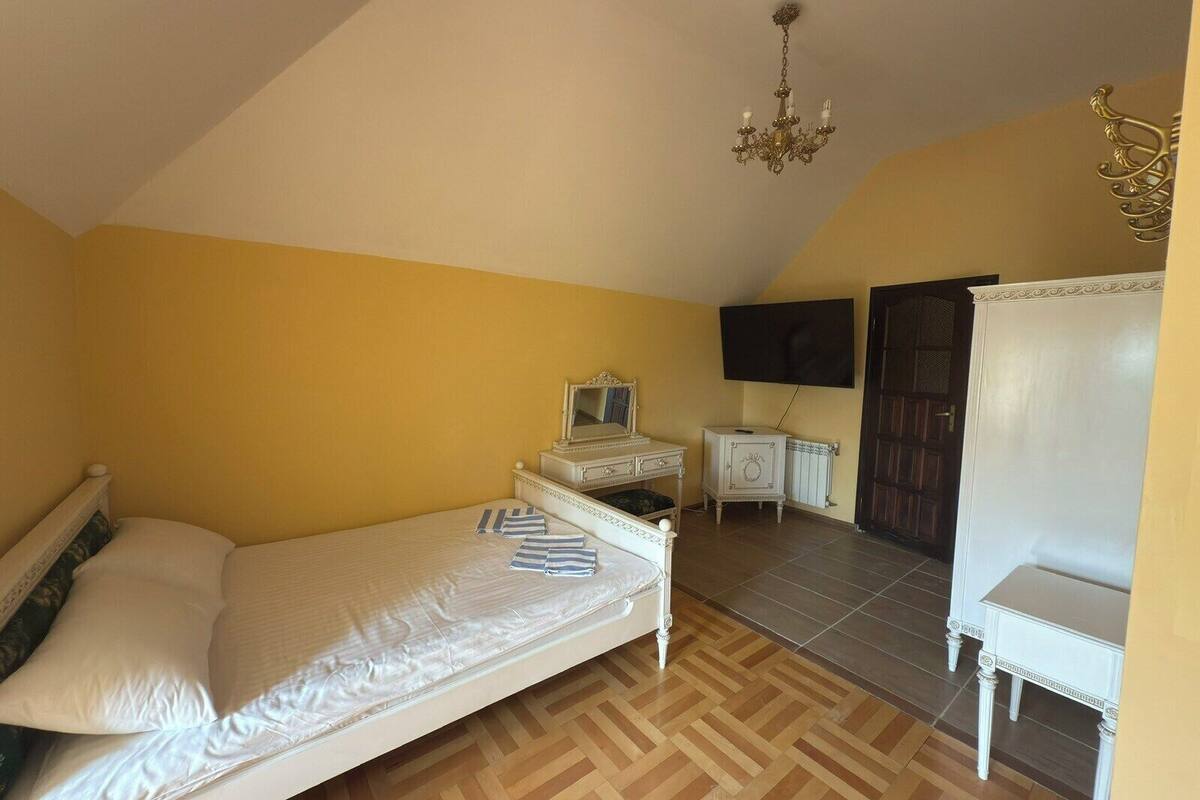 A bedroom with a bed, a dresser, a vanity, a television, and a chair.