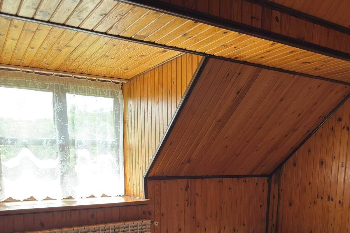 A small, wooden-paneled room with a single bed, a window with sheer curtains, and a radiator under the window.
