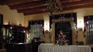 Een warm verlichte kamer met een houten plafond, een kroonluchter, een kerstboom en een gedekte tafel.