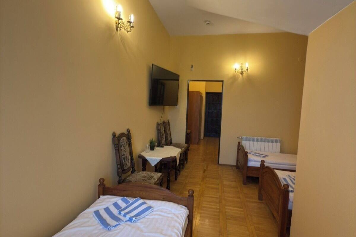 A bedroom with two single beds, a wooden floor, a TV mounted on the wall, and a small dining area with a table and chairs.