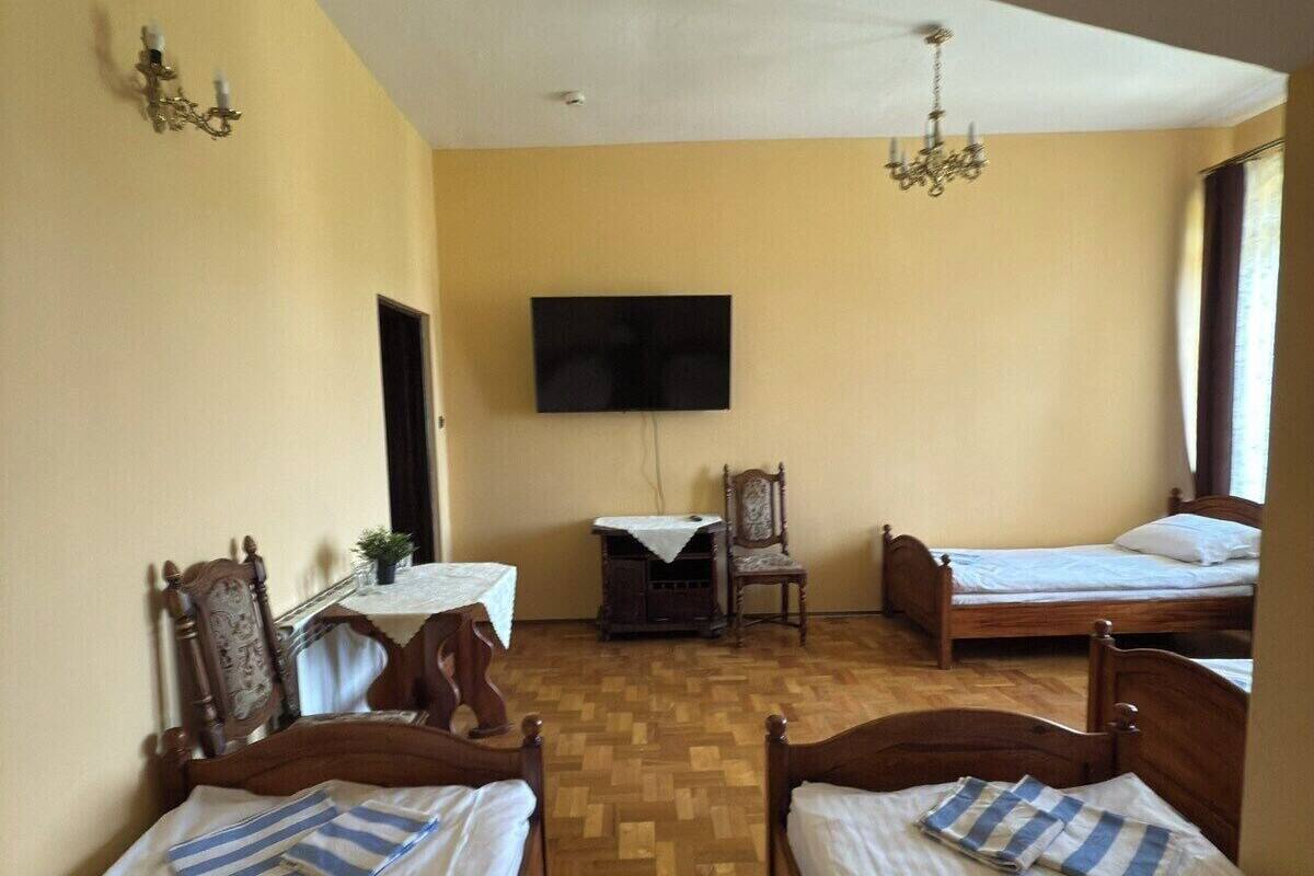 A room with two wooden beds, a television mounted on the wall, a small table with a chair, and a chandelier.