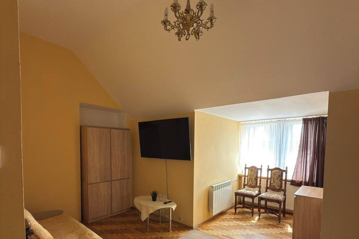 A spacious living room with a high ceiling, a chandelier, a television, and a dining area with chairs and a table.