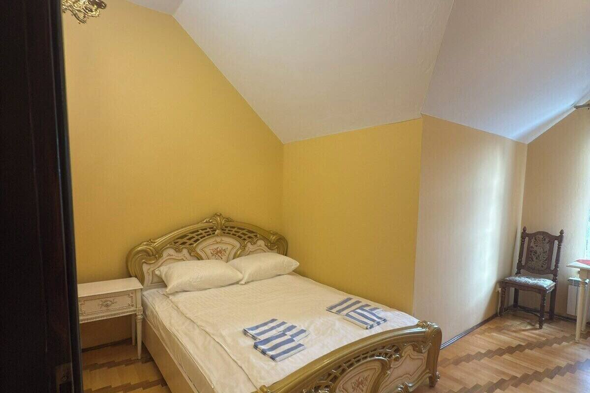 A bedroom with a wooden herringbone floor, a bed with ornate headboard, and a nightstand.