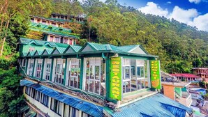 A restaurant with a green roof and multiple windows, surrounded by lush greenery and hills. - Punsisi Resort - Delhousie Adamspeak (Nallathanniya)