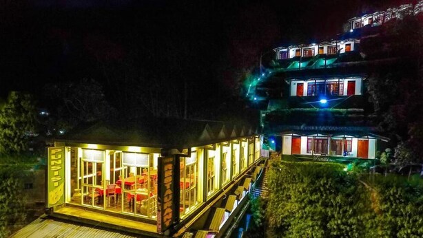 A multi-story building with illuminated windows and a dining area visible through the glass. - Punsisi Resort - Delhousie Adamspeak (Nallathanniya)