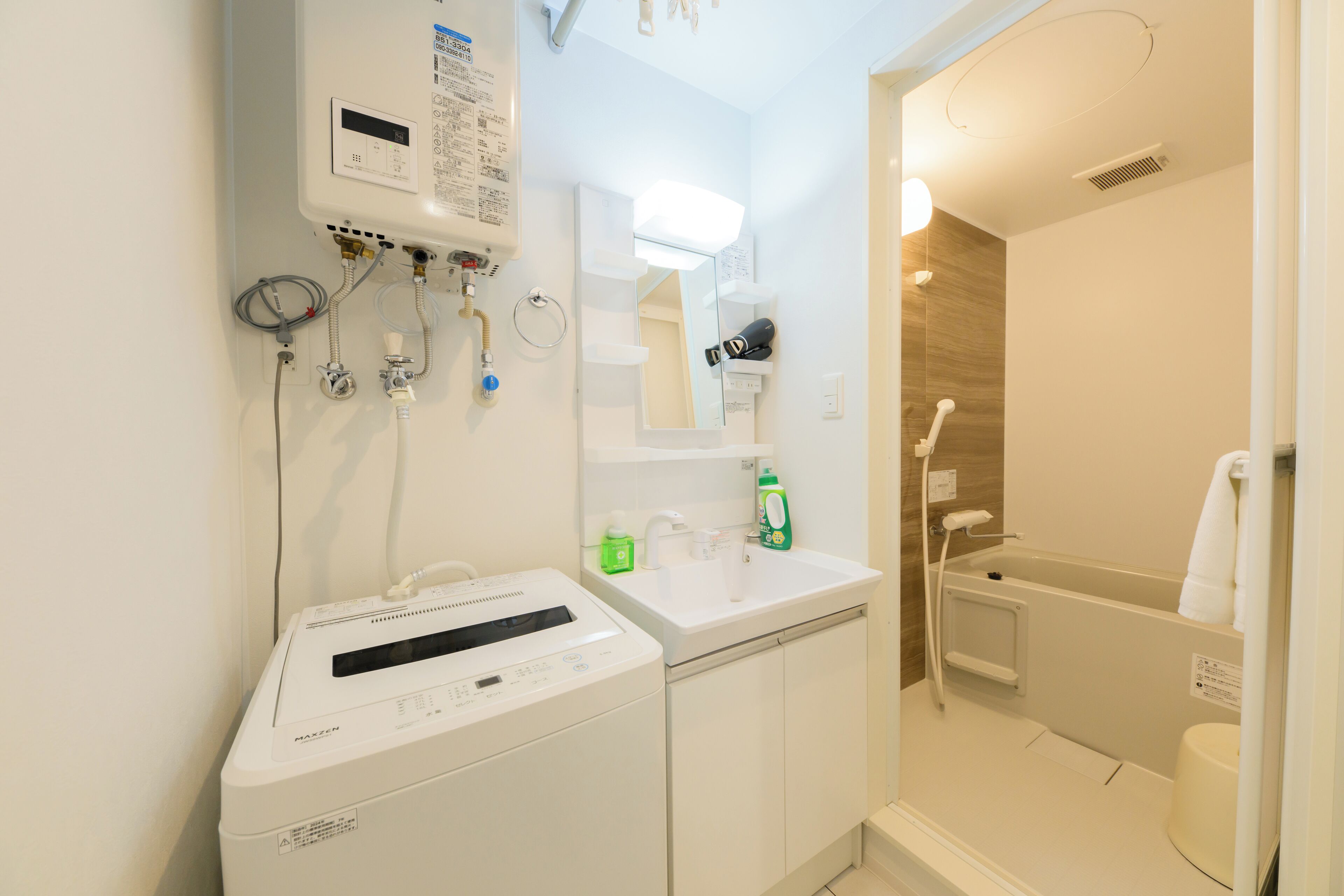 Un baño moderno con lavadora integrada, un lavamanos, un espejo y una zona de ducha.