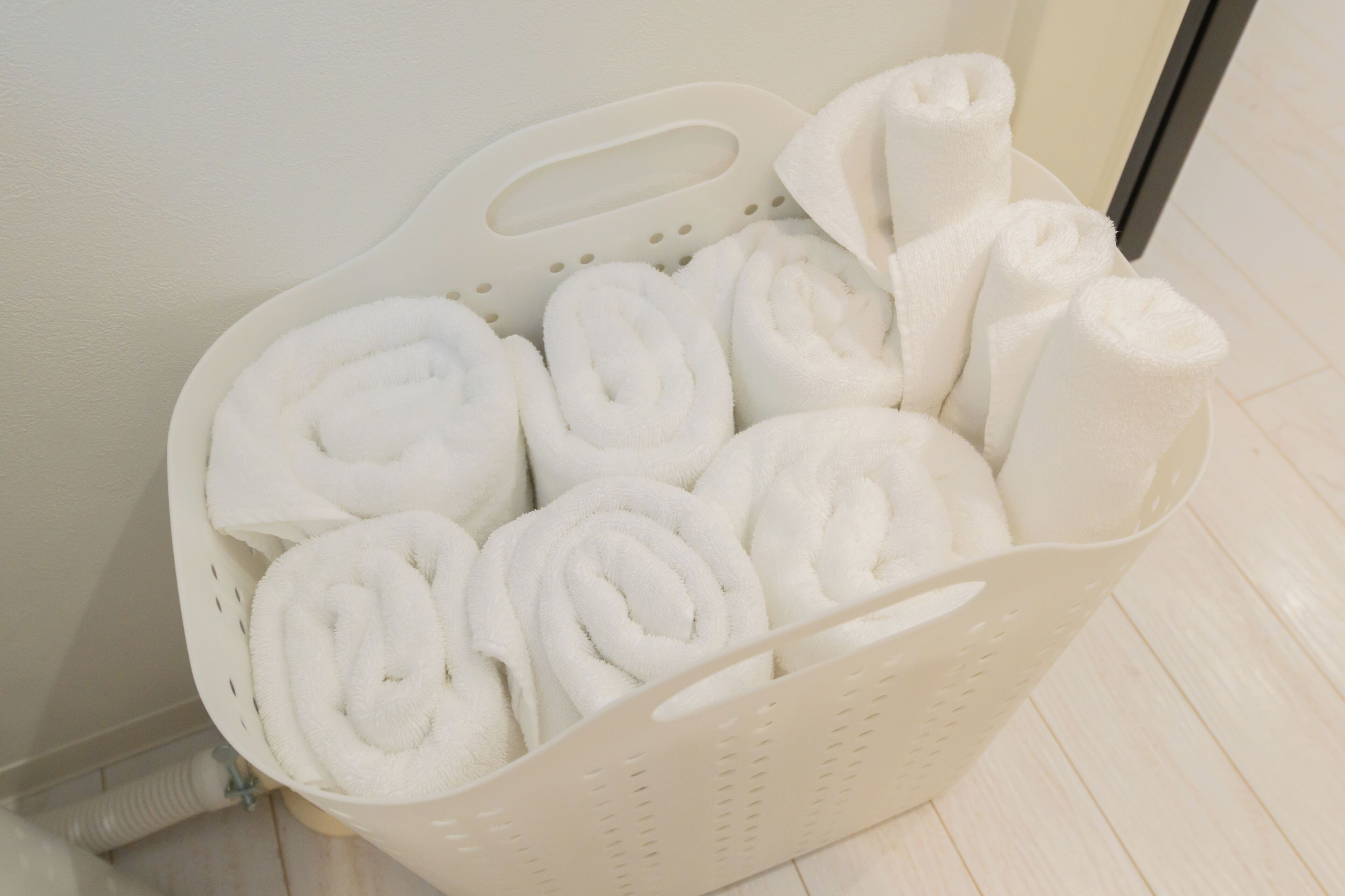 A white plastic basket filled with neatly rolled white towels.