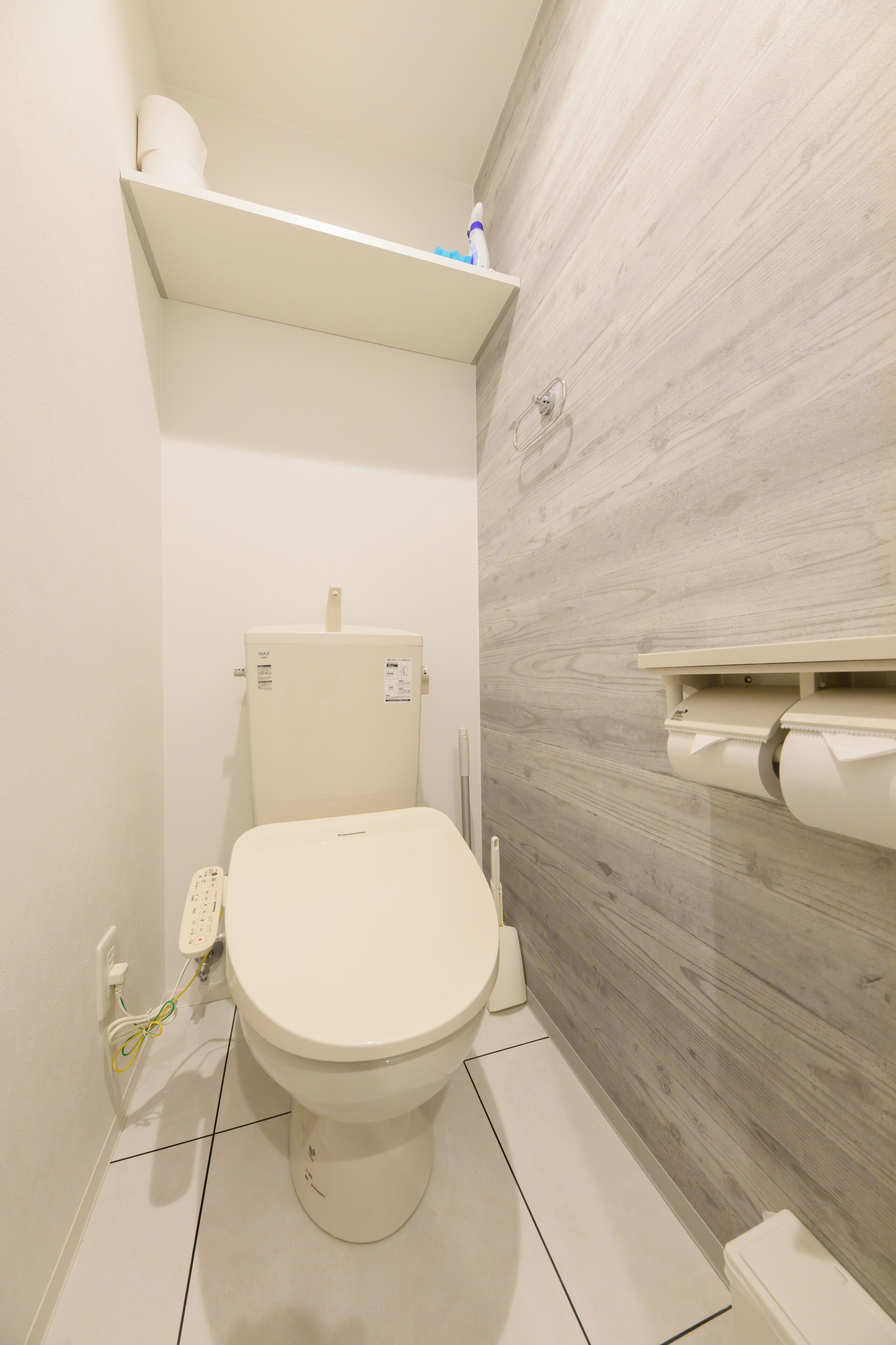 A small, modern bathroom with a toilet, a shelf above the toilet, and a toilet paper holder on the wall.