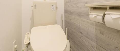 A small, modern bathroom with a toilet, a shelf above the toilet, and a toilet paper holder on the wall.