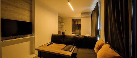 A modern living room with a flat-screen TV, a wooden coffee table, and a sofa with cushions.
