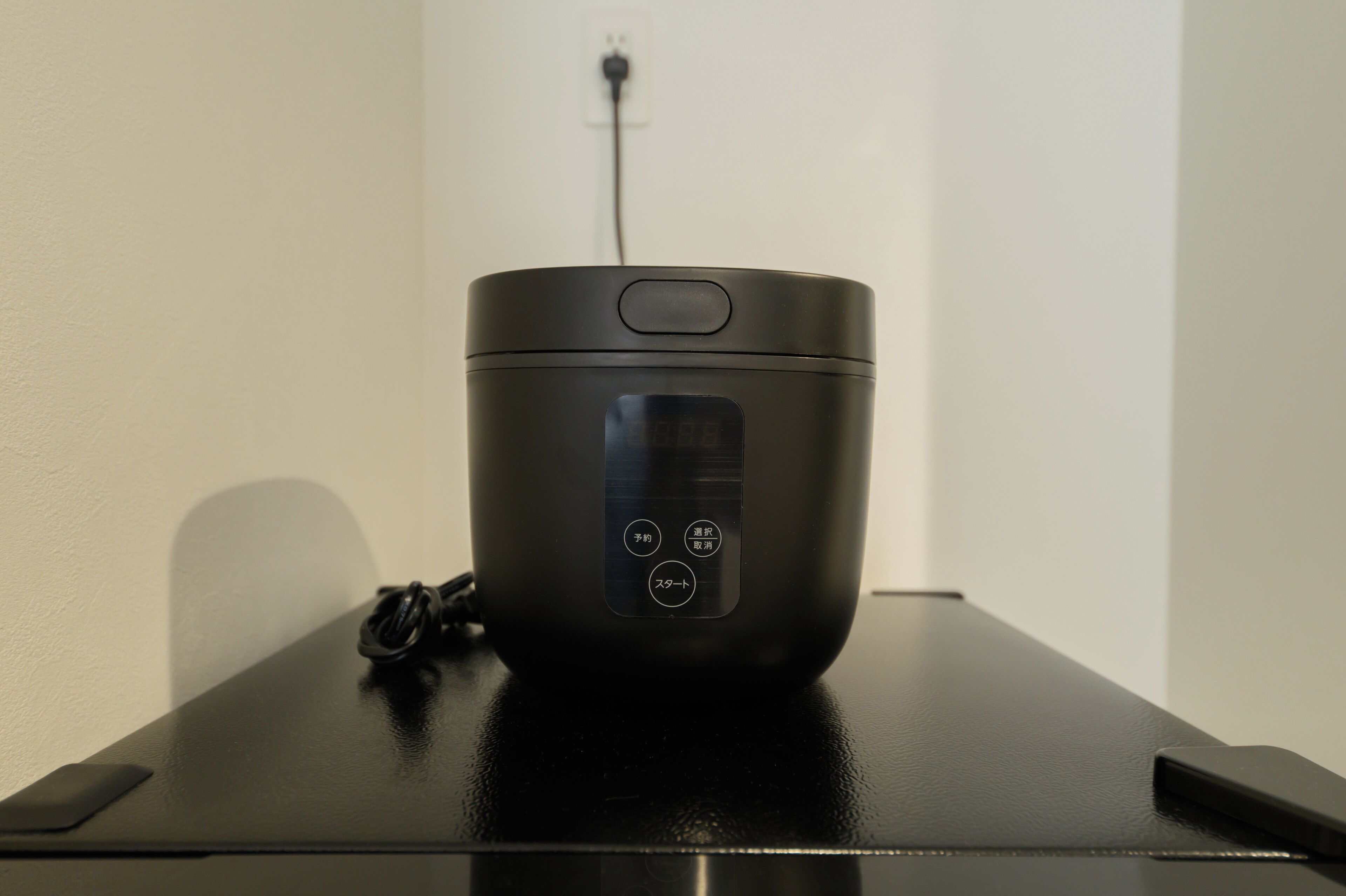 Un altavoz portátil negro sobre una mesa negra, con un cable de alimentación conectado.