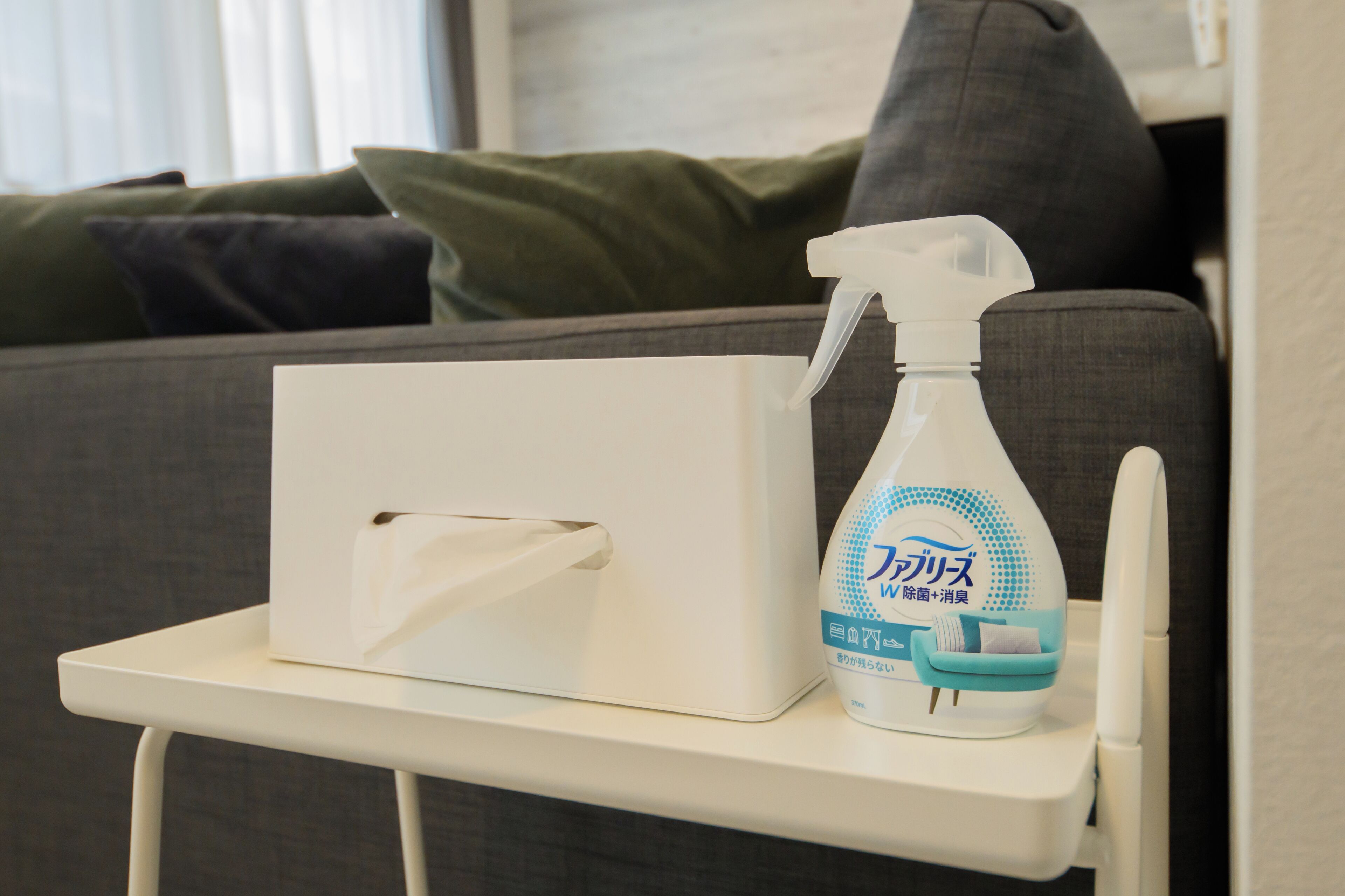 A tissue box and a spray bottle on a small white table.