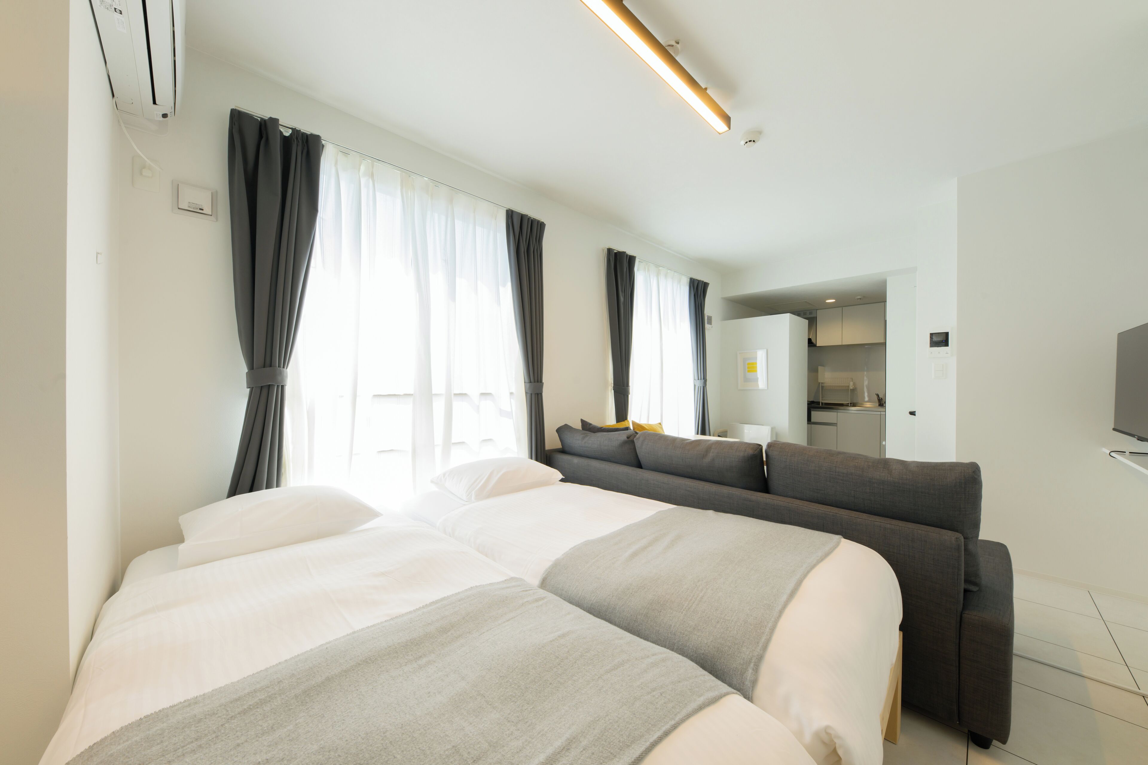 A modern hotel room with a large bed, a sofa, and a kitchenette in the background.
