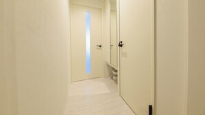 A hallway with a door leading to a bathroom, a large mirror, and a light-colored floor. - EFFECT Kikusui (Sapporo)