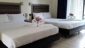Habitación de hotel con dos camas, cada una con sábanas y almohadas blancas. Hay toallas decorativas sobre las camas y un jarrón con flores en la mesita de noche.