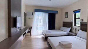 Habitación de hotel con dos camas, un escritorio, un televisor y una ventana con cortinas.