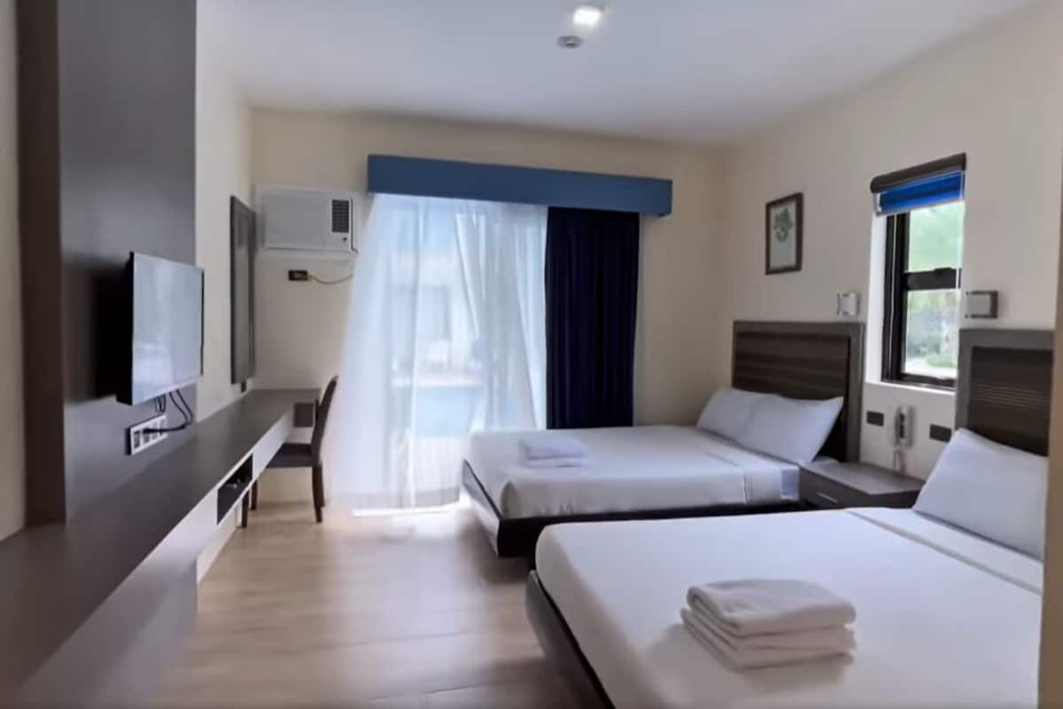 Habitación de hotel con dos camas, un escritorio, un televisor y una ventana con cortinas.