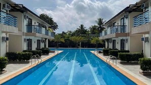 Una piscina flanqueada por edificios de dos pisos, rodeada de follaje y palmeras.