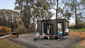A small cabin with a fire pit, seating, and an air conditioning unit. - Churinga Orchards by Tiny Away (Lenswood)