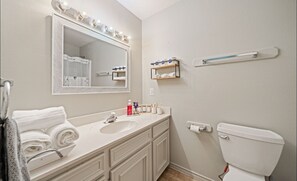 A bathroom with a white sink, vanity, and mirror with lights. There are towels and toiletries on the counter. - Ocean Village Retreat , Walk to Beach+Private Dock (Corpus Christi)