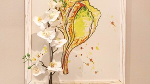 Ein gerahmtes Kunstwerk mit einer Muschel und weißen Orchideen, platziert auf einem weißen Regal.