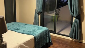 Ein Schlafzimmer mit einem Bett, einem Nachttisch, einem Deckenventilator und einer Schiebetür, die auf einen Balkon führt.