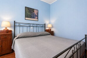 Un dormitorio con una cama, dos mesitas de noche, un velador, un cuadro en la pared y una lámpara de techo.