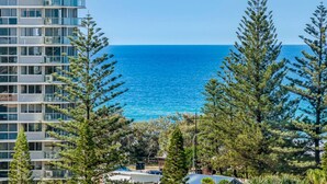 A coastal view with a modern building, clear blue sea, and surrounding pine trees.