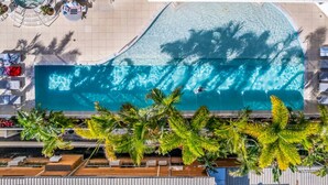 An aerial view of a swimming pool with a curved edge, surrounded by palm trees and lounge chairs.