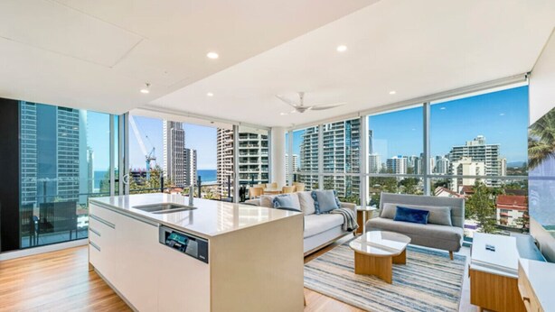 A modern living room with a large island kitchen, large windows with city views, and a minimalist design.