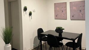 Un espace repas comprenant une table rectangulaire, quatre chaises noires et deux tableaux accrochés au mur.