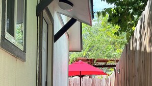 Un pequeño patio exterior con valla de madera, una sombrilla roja y una mesa con sillas.