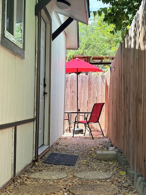A narrow outdoor patio with a wooden fence, a red umbrella, and a table with chairs.