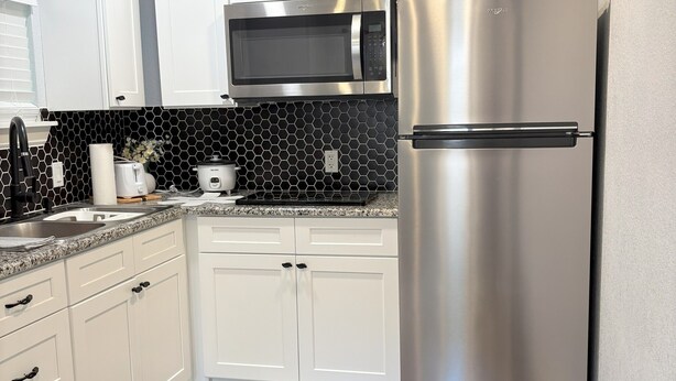 Una cocina moderna con alacenas blancas, un refrigerador de acero inoxidable, un microondas y un lavaplatos.