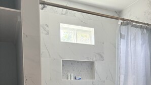 Un baño con paredes de mármol, ducha con cortina y un estante con artículos de aseo.