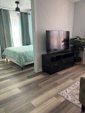 A modern bedroom with a bed, a flat-screen TV, a black entertainment unit, and a potted plant.
