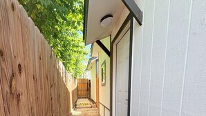 Un estrecho sendero con una cerca de madera en un lado y una pared blanca en el otro, que conduce a una puerta.