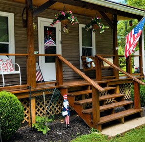 A wooden porch with a welcome sign, a gnome figure, and an American flag.