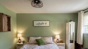 A bedroom with a bed, two bedside tables with lamps, a dresser, a framed picture on the wall, and a window with curtains.