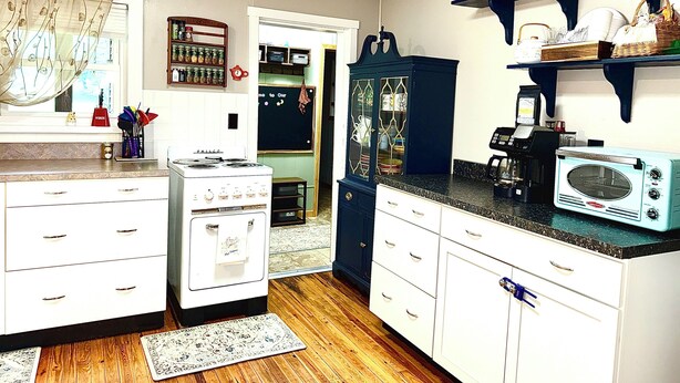 A kitchen with white cabinetry, a vintage stove, a microwave, and a coffee maker.