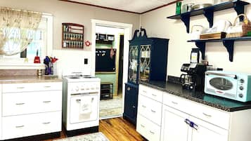 A kitchen with white cabinetry, a vintage stove, a microwave, and a coffee maker.