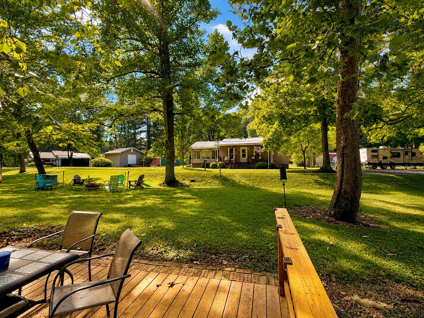 Une terrasse avec des chaises et une table, entourée d’une pelouse verdoyante et d’arbres.