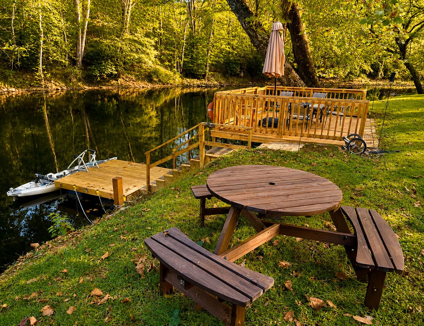 Eine Holzterrasse mit Tisch und Bänken, ein Boot an der Anlegestelle und bewaldete Hügel im Hintergrund.