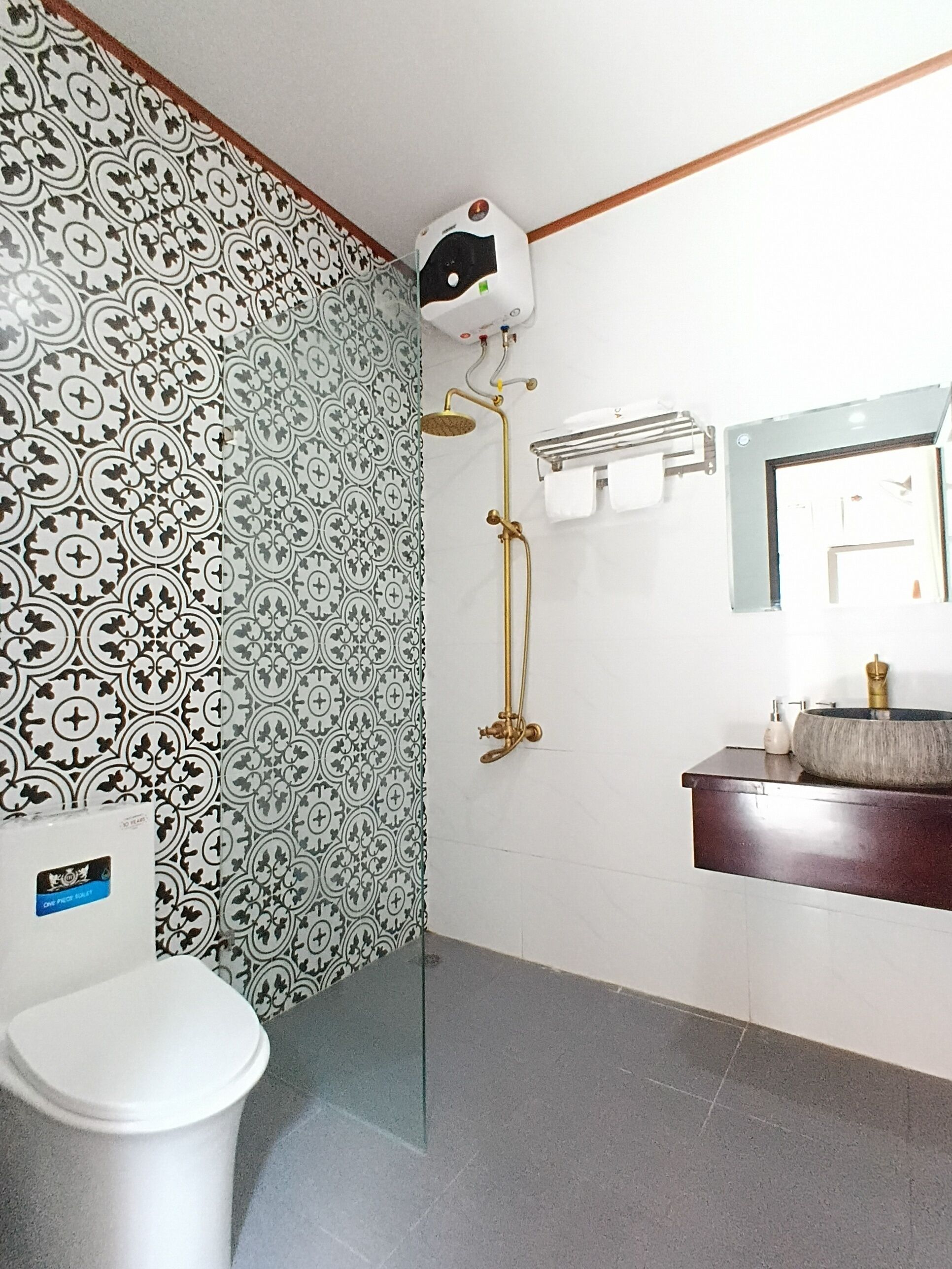 A bathroom with patterned wallpaper, a toilet, a shower with a golden showerhead, and a sink with a round basin.