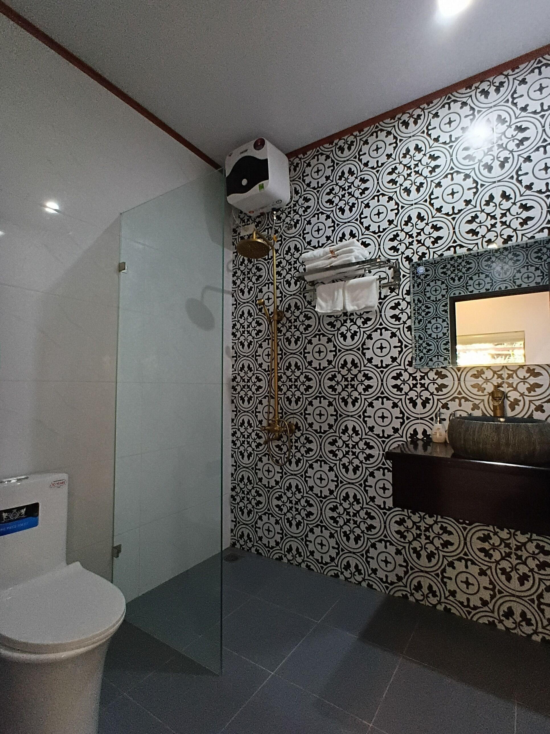 A bathroom with a patterned wall, a glass shower enclosure, a sink with a mirror, and a toilet.