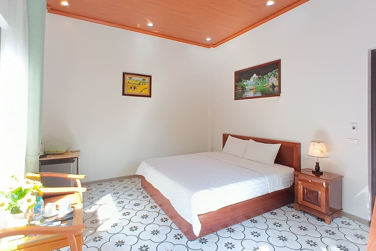A bedroom with a bed, a nightstand, a lamp, and two wall-mounted pictures.