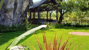 Ein Gazebo mit einem Ziegeldach, umgeben von üppiger Vegetation und einer großen Felsformation.